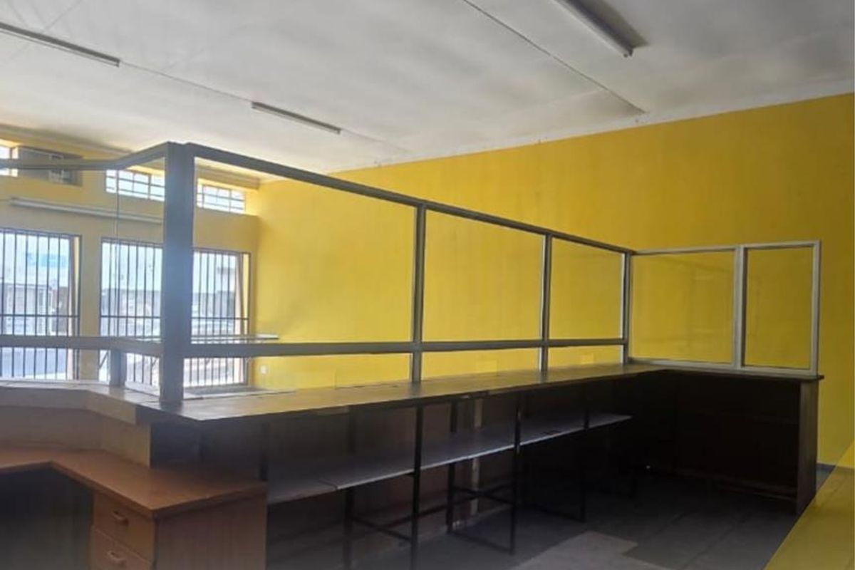 An empty office space featuring a built-in reception counter with a glass partition, fluorescent lighting, and security bars on the windows.