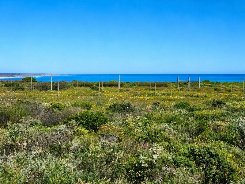 A scenic view of the coastline and ocean from a vacant residential plot, featuring natural vegetation and perimeter wire fencing.