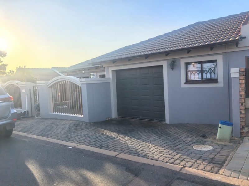 Front exterior view of the property featuring a paved driveway, single garage, and secure boundary wall with metal gate.
