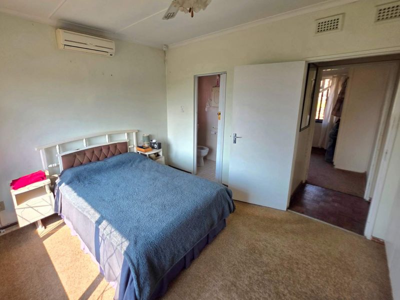 A bedroom featuring carpet flooring, a ceiling fan, and a wall-mounted air conditioning unit, with direct access to an en-suite bathroom.