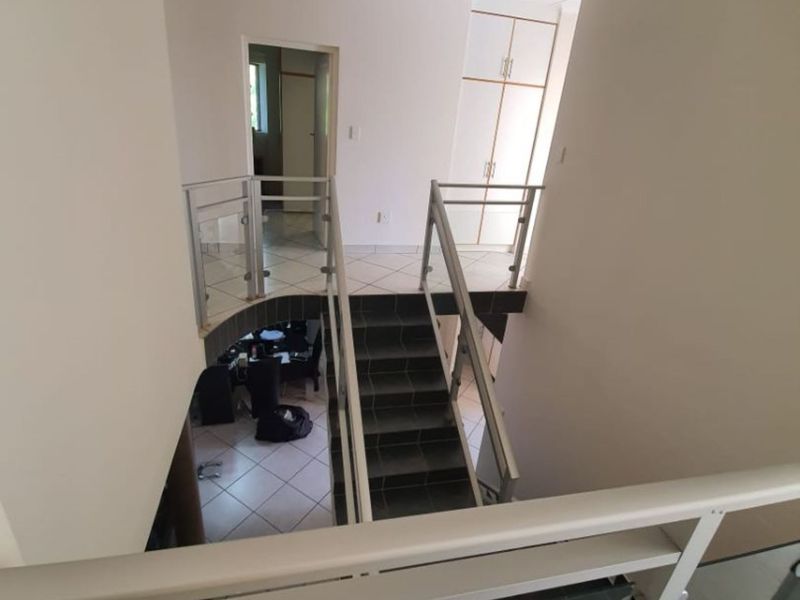 A bright landing area featuring a staircase with a modern glass balustrade, tiled flooring, and built-in storage cupboards.