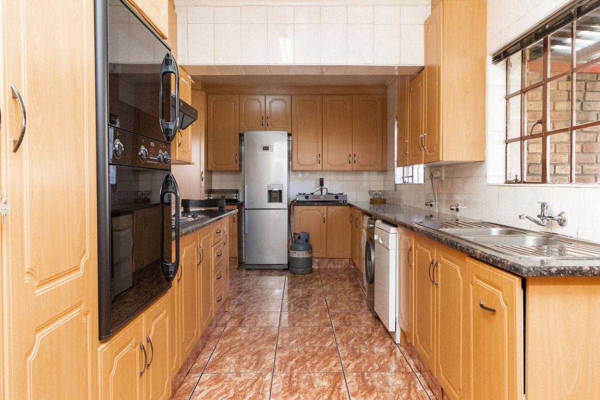 A functional kitchen featuring light wood cabinetry, granite countertops, double stainless steel sink, and built-in oven, with tiled flooring throughout.