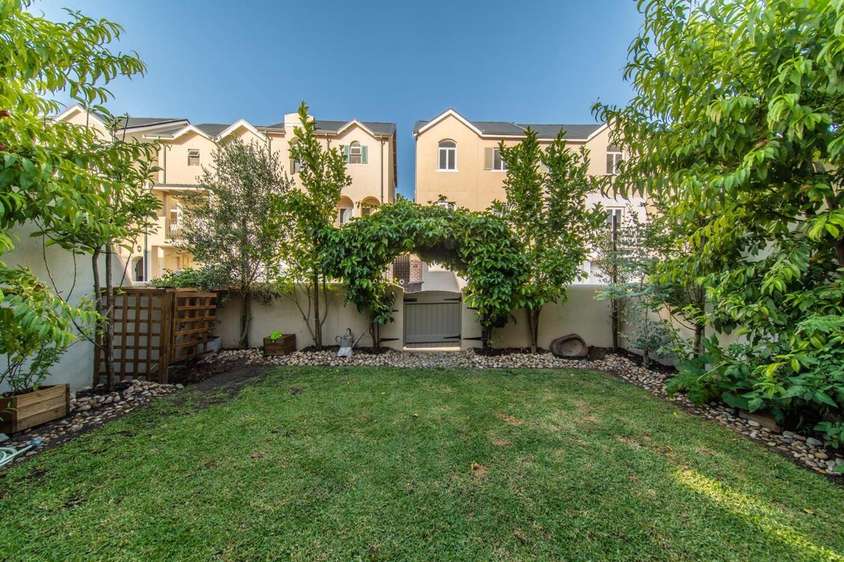A well-maintained rear garden featuring a manicured lawn, established trees, a decorative arched trellis, and a secure pedestrian gate.