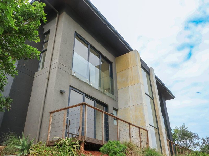 Modern multi-story rear facade featuring a timber deck, glass balustrades, and a prominent stone-clad feature wall with large windows.