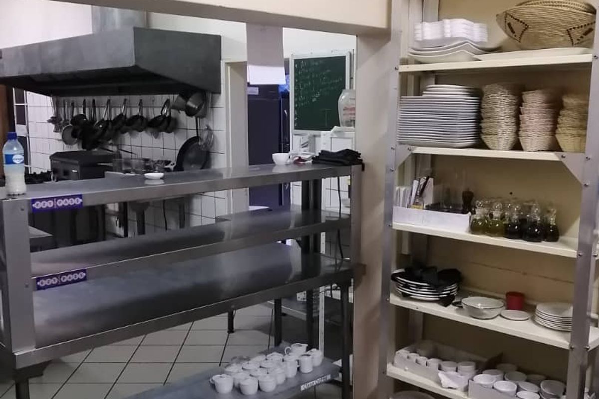 A commercial kitchen prep and storage area featuring stainless steel shelving, a professional extractor hood, and tiled flooring.