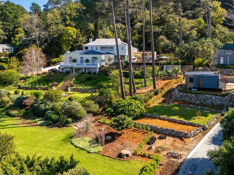 Aerial view of a large multi-level residential property featuring extensive terraced gardens, stone retaining walls, and a paved driveway set against a wooded backdrop.