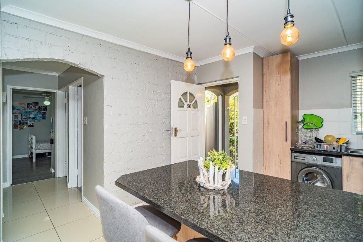 A modern kitchen featuring granite countertops, built-in cabinetry, and stylish pendant lighting, with an open-plan layout leading to the entrance and hallway.
