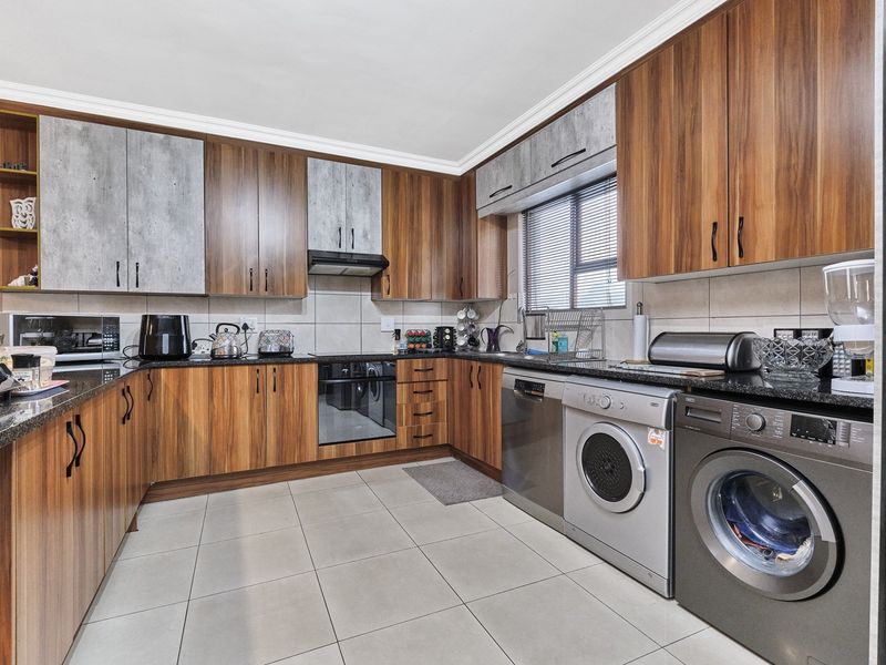 Modern kitchen featuring wood-grain and concrete-look cabinetry, granite countertops, integrated oven, extractor fan, and tiled flooring with space for laundry appliances.