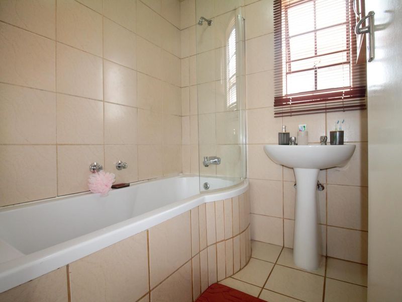 A functional bathroom featuring a pedestal basin, a bathtub with a glass shower screen, and neutral wall and floor tiling.