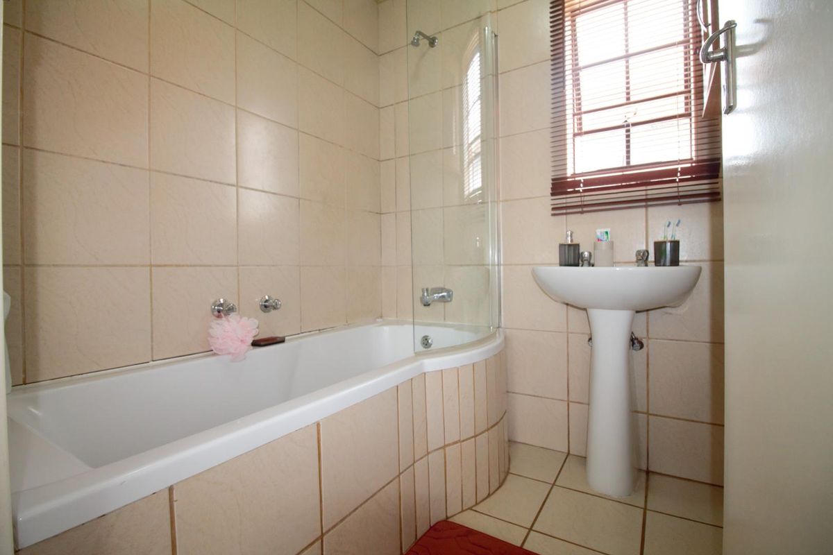 A functional bathroom featuring a pedestal basin, a bathtub with a glass shower screen, and neutral wall and floor tiling.