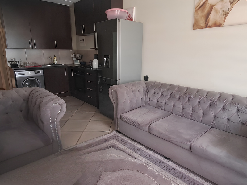 Open-plan living area featuring a compact kitchen with dark cabinetry and tiled flooring, seamlessly connected to the lounge space.