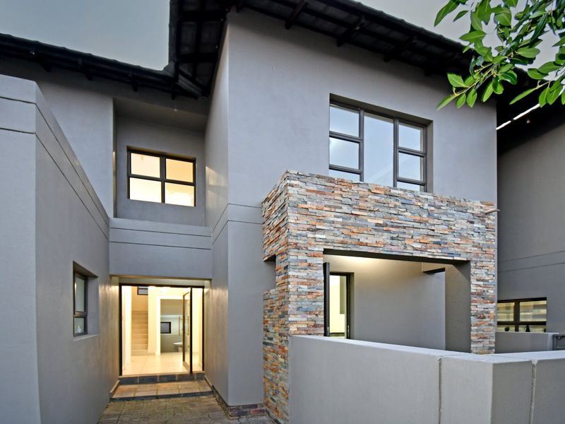 Modern double-storey home entrance featuring contemporary grey plaster finish, decorative stone cladding, and clean architectural lines.