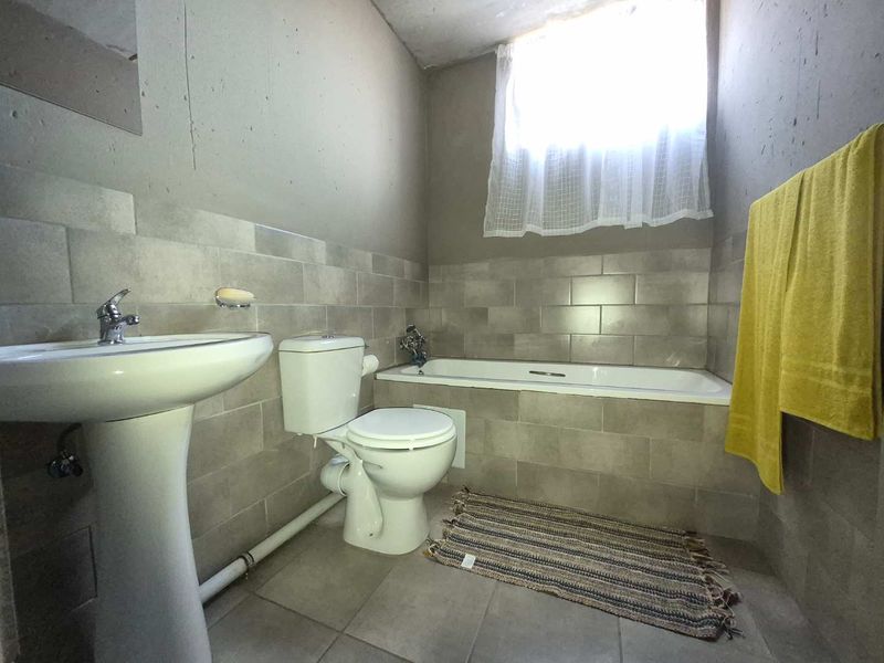 A functional bathroom featuring a pedestal basin, toilet, and bathtub with neutral wall tiling and natural light from a window.