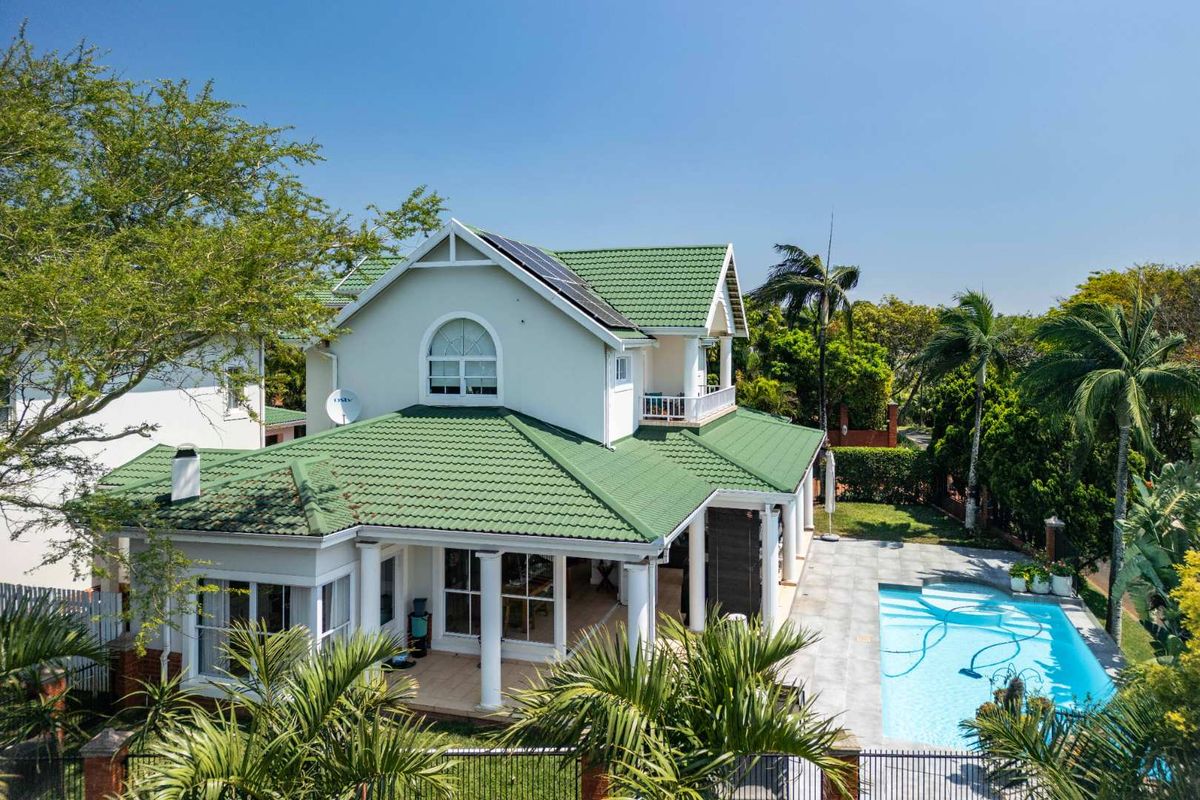 Aerial view of the rear exterior featuring a swimming pool, covered patio, balcony, and a well-maintained tiled roof with solar panels.