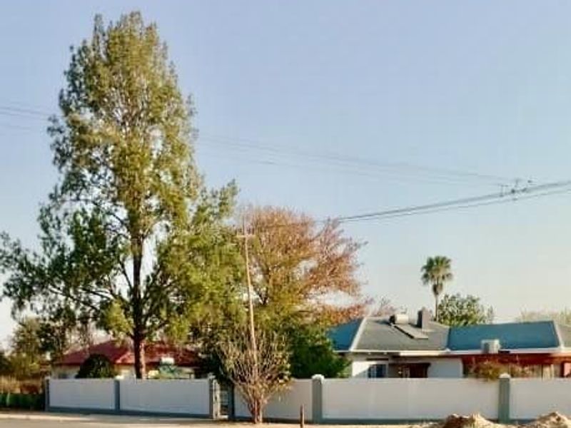Street view of the property featuring a secure perimeter wall, pitched roofline, and solar geyser installation.