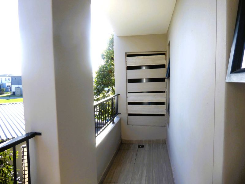 A covered balcony featuring tiled flooring, a metal balustrade, and a fixed privacy screen, offering an outdoor space with neighborhood views.