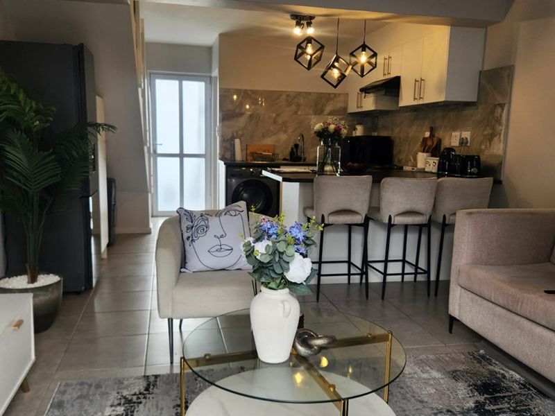 An open-plan living and kitchen area featuring modern cabinetry, a stone-look backsplash, breakfast bar seating, and tiled flooring throughout.