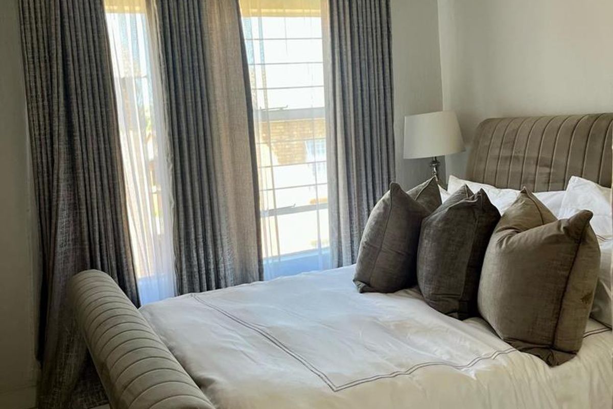 A well-maintained bedroom featuring neutral wall finishes, crown molding, and large windows with fitted curtain tracks.