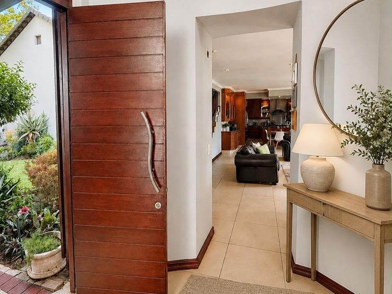 Welcoming entrance foyer featuring a large solid timber pivot door, neutral tiled flooring, and a clear view through to the open-plan living area.