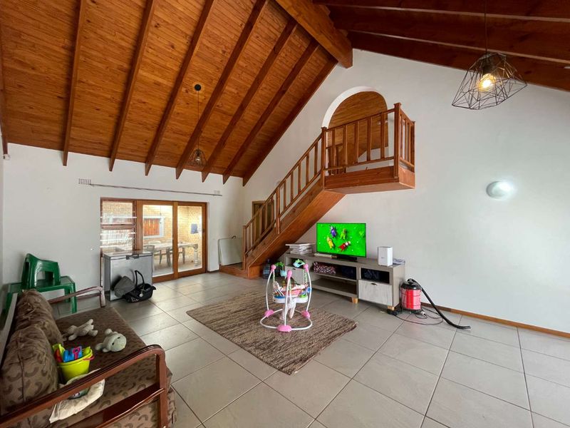 Spacious living area featuring a high vaulted timber ceiling, exposed beams, tiled flooring, and a timber staircase leading to an upper level.