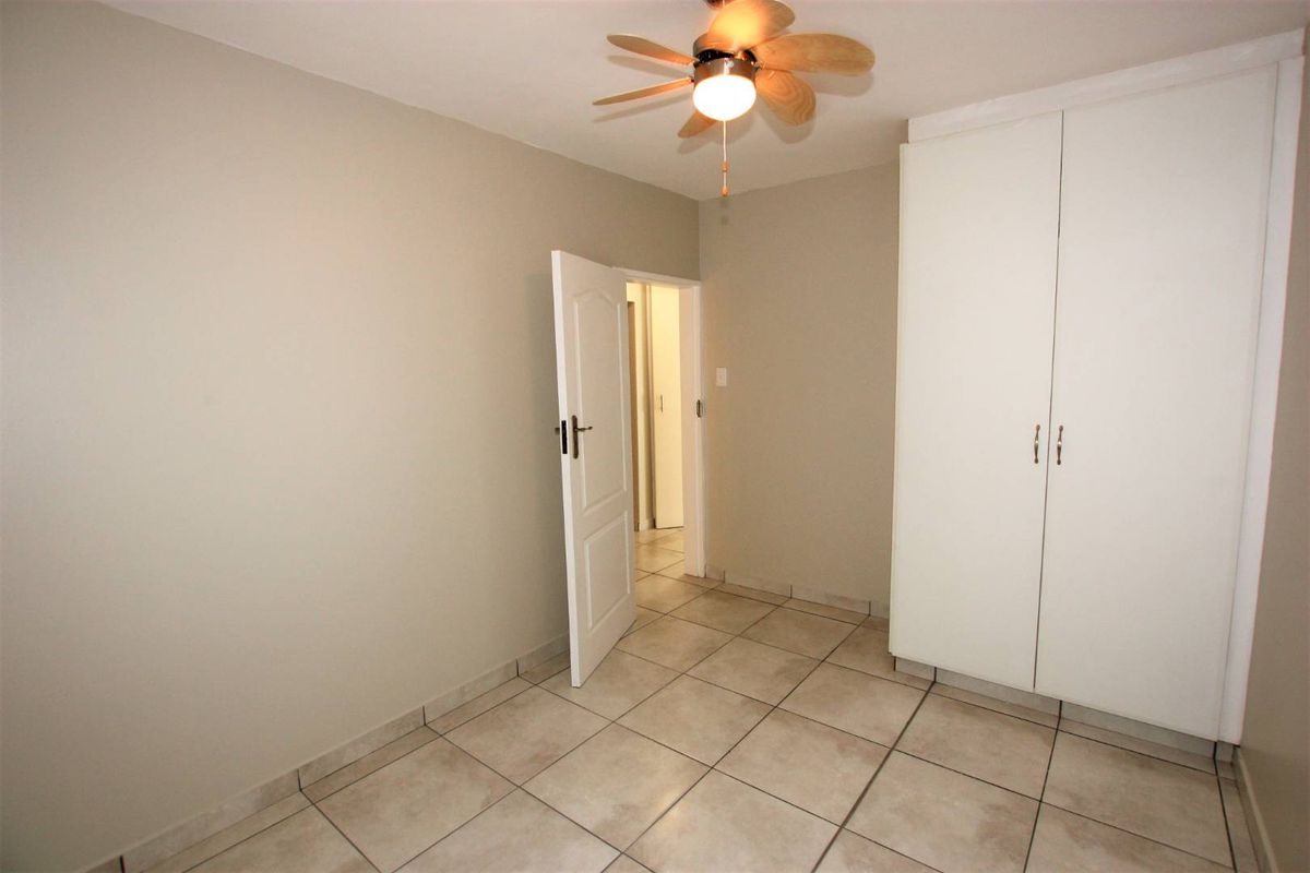 A clean, empty bedroom featuring neutral wall tones, tiled flooring, a ceiling fan, and a built-in wardrobe for storage.