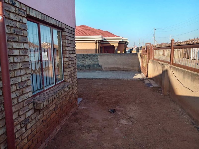 A view of the rear yard area featuring face brick exterior walls, a paved driveway section, and perimeter walling with a metal security gate.