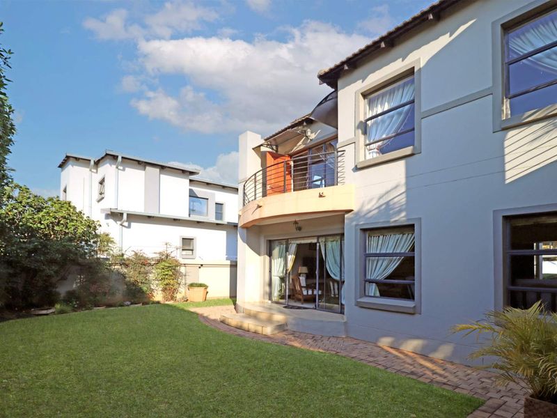 Rear view of the double-story house featuring a private garden, brick paved pathway, and an upper-level balcony with metal railings.