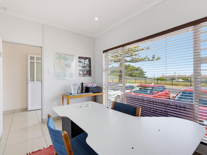 A bright office space featuring tiled flooring, recessed lighting, and large windows with venetian blinds, offering a functional workspace environment.