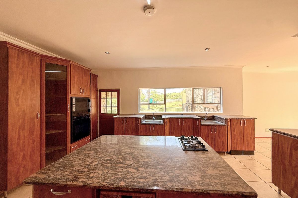Spacious kitchen featuring extensive wooden cabinetry, granite countertops, a central island with a gas hob, and double sinks with garden views.