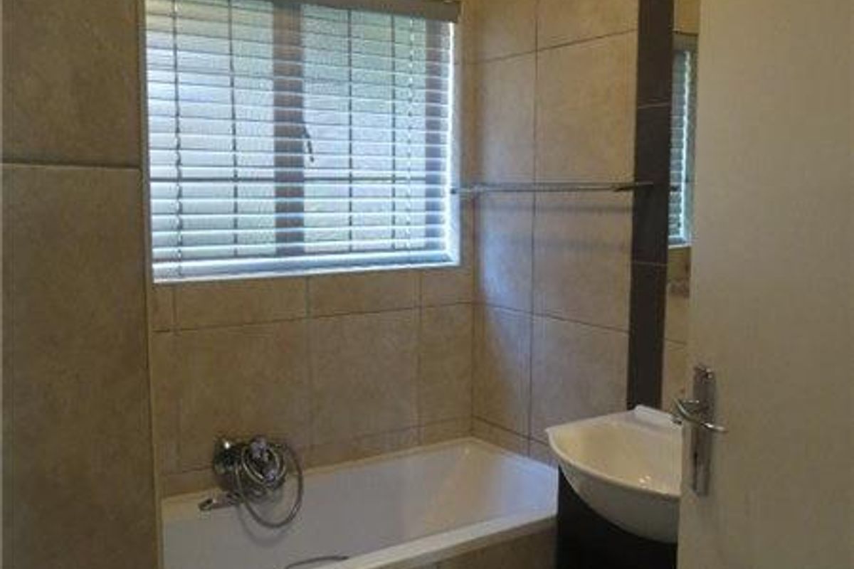 A compact bathroom featuring tiled walls, a bathtub with a mixer tap, a wall-mounted basin, and a toilet.