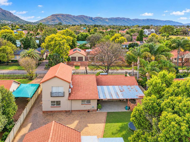 Aerial view of a residential property featuring a terracotta tiled roof, paved driveway, and a covered patio area with mountain views in the background.