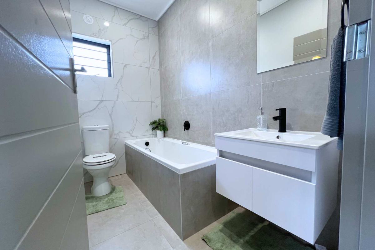 Modern bathroom featuring a built-in bathtub, wall-mounted vanity with basin, and contemporary matte black fixtures, finished with large-format neutral wall and floor tiles.
