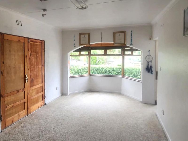 An empty living room featuring a large bay window, carpeted flooring, and classic double wooden doors, offering a blank canvas for interior design.