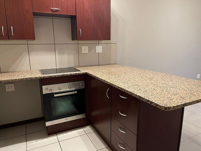 A clean, functional kitchen featuring dark wood cabinetry, granite countertops, a built-in oven, and an electric hob with a tiled backsplash.