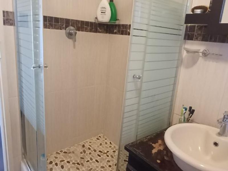 A compact bathroom featuring a glass-enclosed shower with pebble-style floor tiling and a vanity unit with a basin.