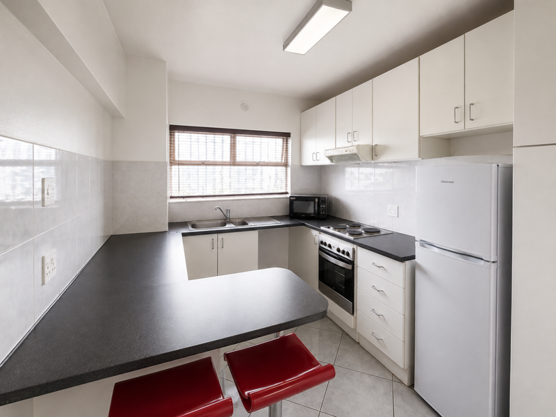 A functional kitchen featuring white cabinetry, dark laminate countertops, a tiled backsplash, and integrated appliances including an oven and hob.