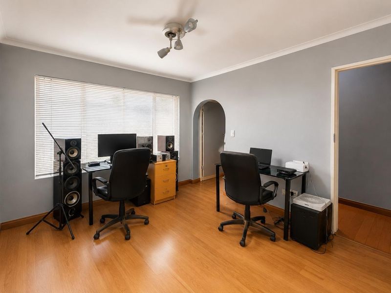 A functional home office space featuring laminate flooring, an arched doorway, and natural light through venetian blinds.