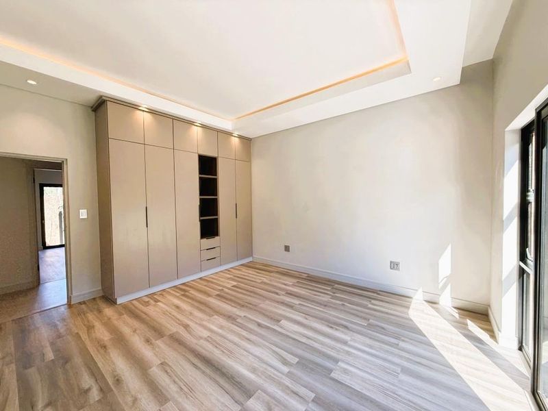 A bright, modern bedroom featuring high-quality laminate flooring, extensive built-in cabinetry, and recessed ceiling lighting with access to an outdoor area.