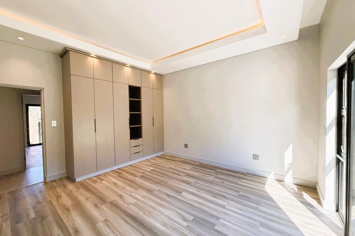 A bright, modern bedroom featuring high-quality laminate flooring, extensive built-in cabinetry, and recessed ceiling lighting with access to an outdoor area.