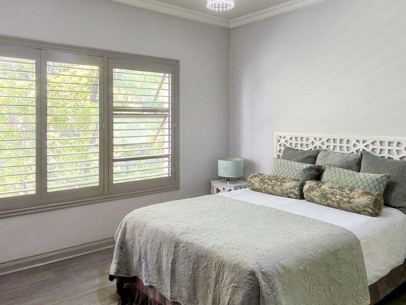 A well-maintained bedroom featuring plantation shutters, crown molding, and modern laminate flooring, offering a clean and neutral living space.