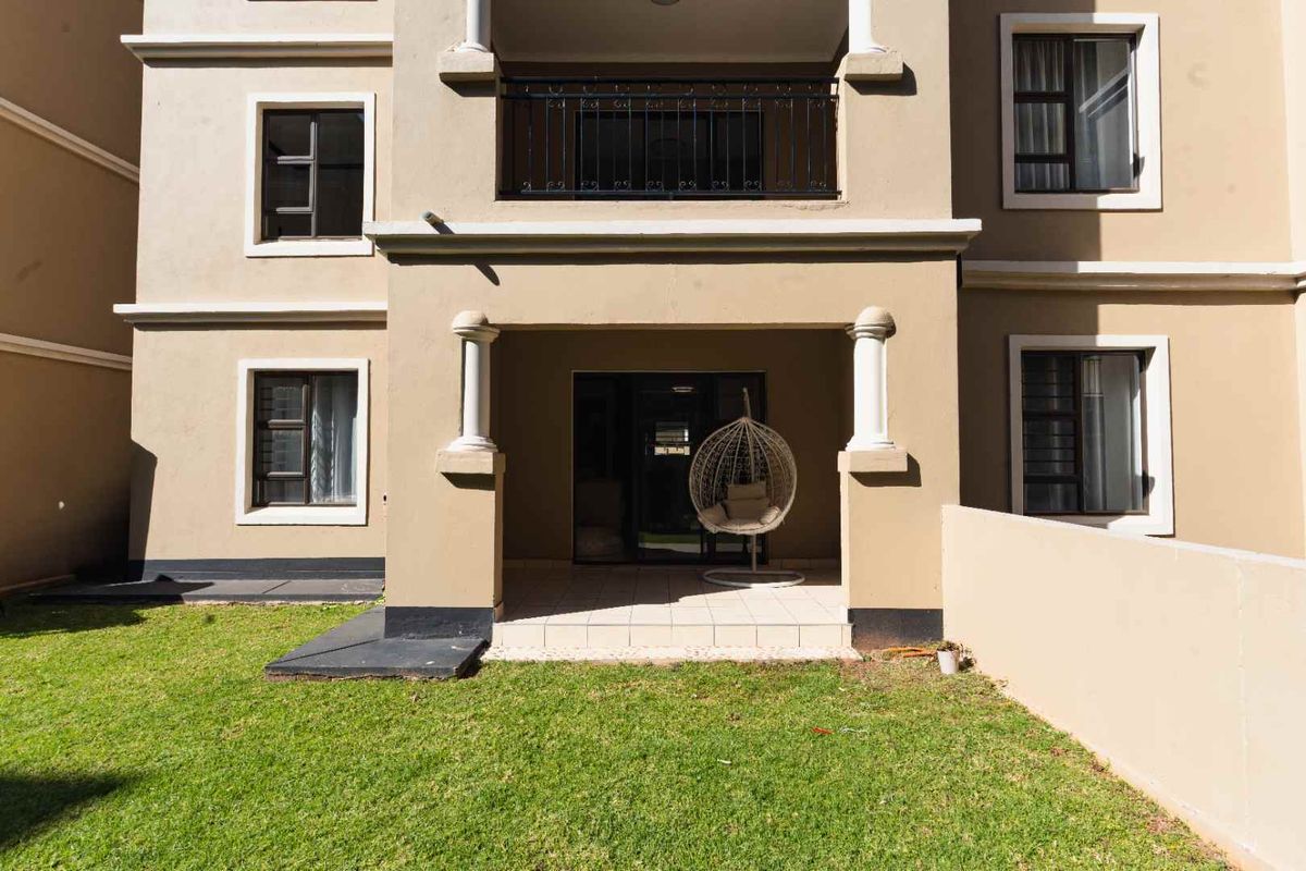 Rear view of the apartment building featuring a ground-floor tiled patio, a first-floor balcony with metal railings, and a private lawn area.