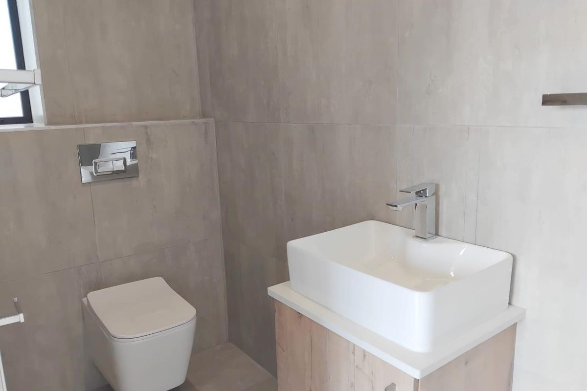 Modern bathroom featuring a wall-mounted toilet with concealed cistern, a contemporary vessel sink on a wooden vanity, and neutral floor-to-ceiling wall tiles.