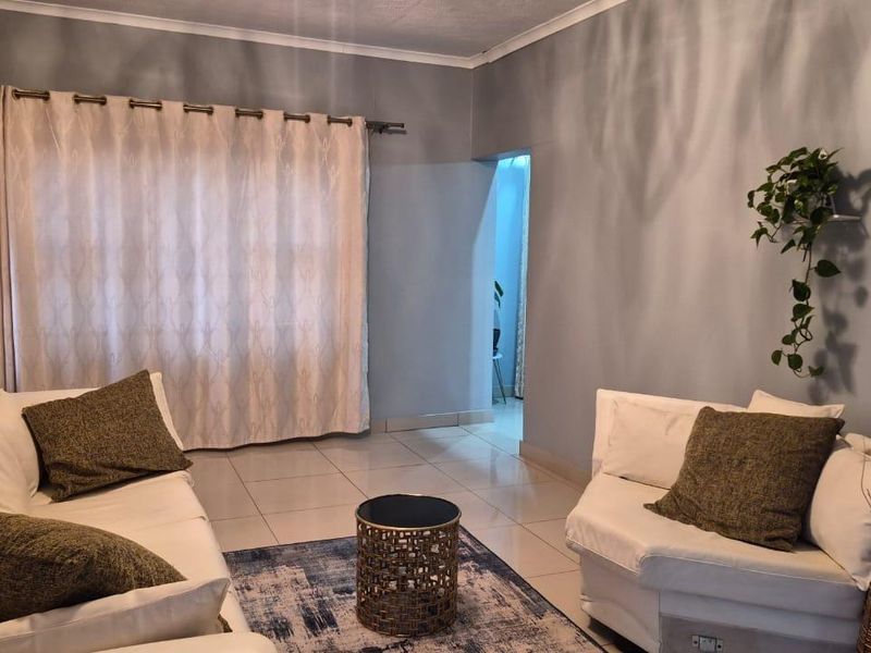 A comfortable living room featuring neutral grey walls, tiled flooring, and large windows dressed with curtains, providing a bright and inviting space.