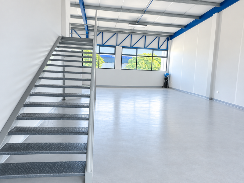 Spacious industrial utility area featuring polished epoxy flooring, exposed blue steel roof trusses, and a metal staircase leading to an upper level.