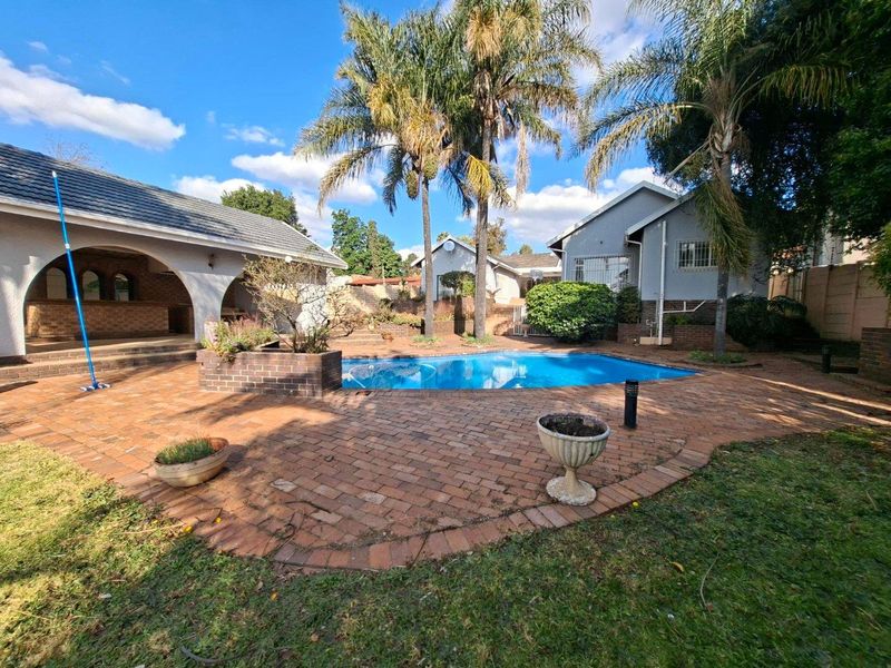 Outdoor entertainment area featuring a swimming pool, brick paved patio, and a covered structure with a built-in bar.