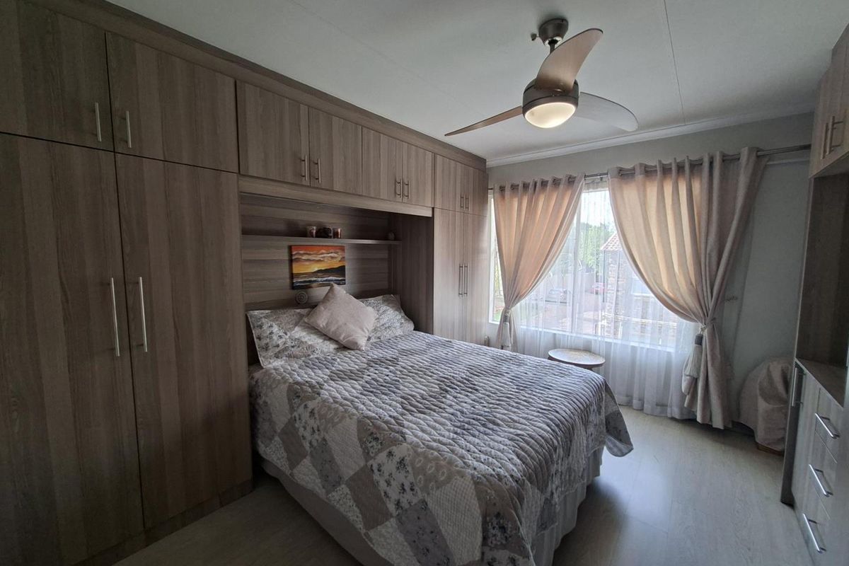 A well-maintained bedroom featuring extensive built-in wooden cabinetry, integrated shelving, and a modern ceiling fan with light fixture.