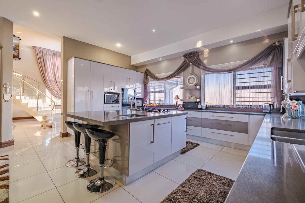 Modern kitchen featuring a central island with stone countertops, integrated cabinetry, built-in oven, and gas hob, adjacent to a staircase with glass balustrades.