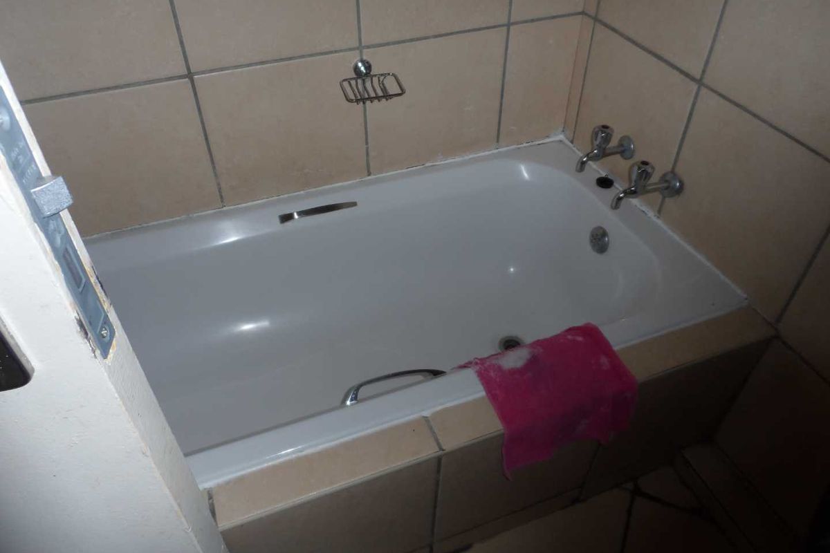 A compact bathroom featuring a built-in bathtub with tiled surround and wall-mounted fixtures, requiring minor maintenance and cosmetic updates.