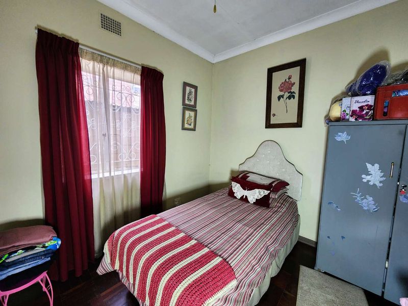 A compact bedroom featuring hardwood flooring, cove cornicing, and a window fitted with security bars.
