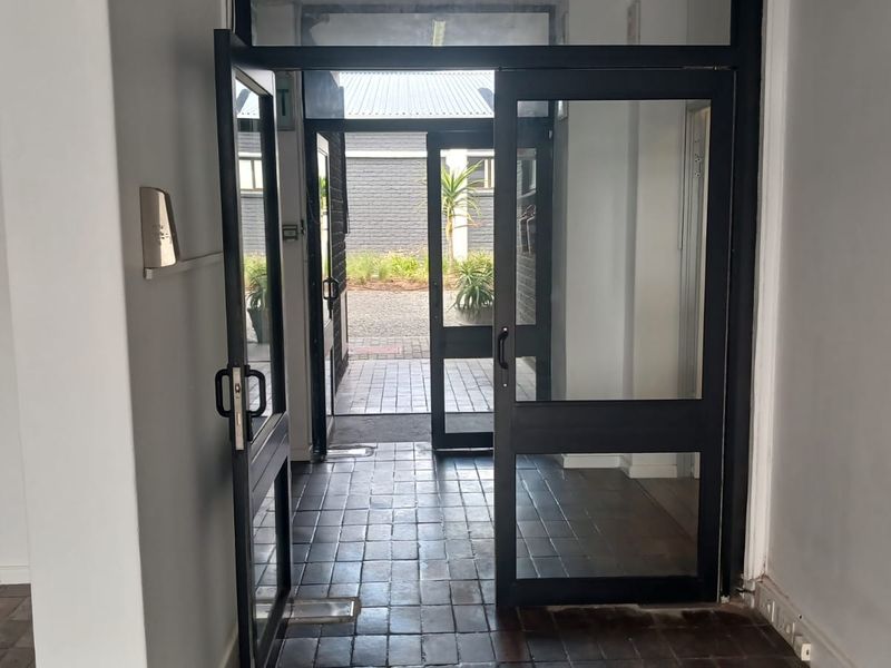 A functional office entrance featuring black aluminium glass doors and tiled flooring, providing direct access to an outdoor paved area.
